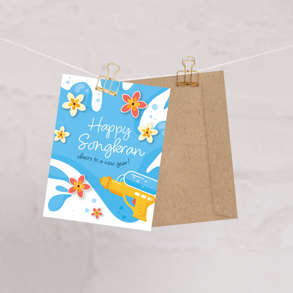 Greeting card with 'Happy Songkran' for Thai New Year with flowers and a water soaking squirt gun on a blue background.
