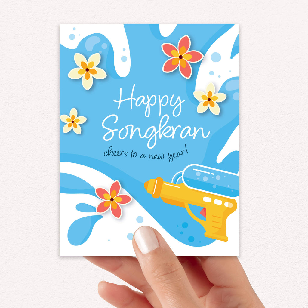 Greeting card with 'Happy Songkran' for Thai New Year with flowers and a water soaking squirt gun on a blue background.