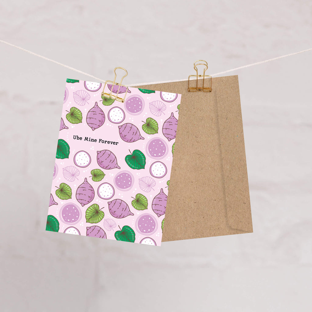 greeting card with a purple and green pattern on a pink background, clipped to a string against a light gray background.