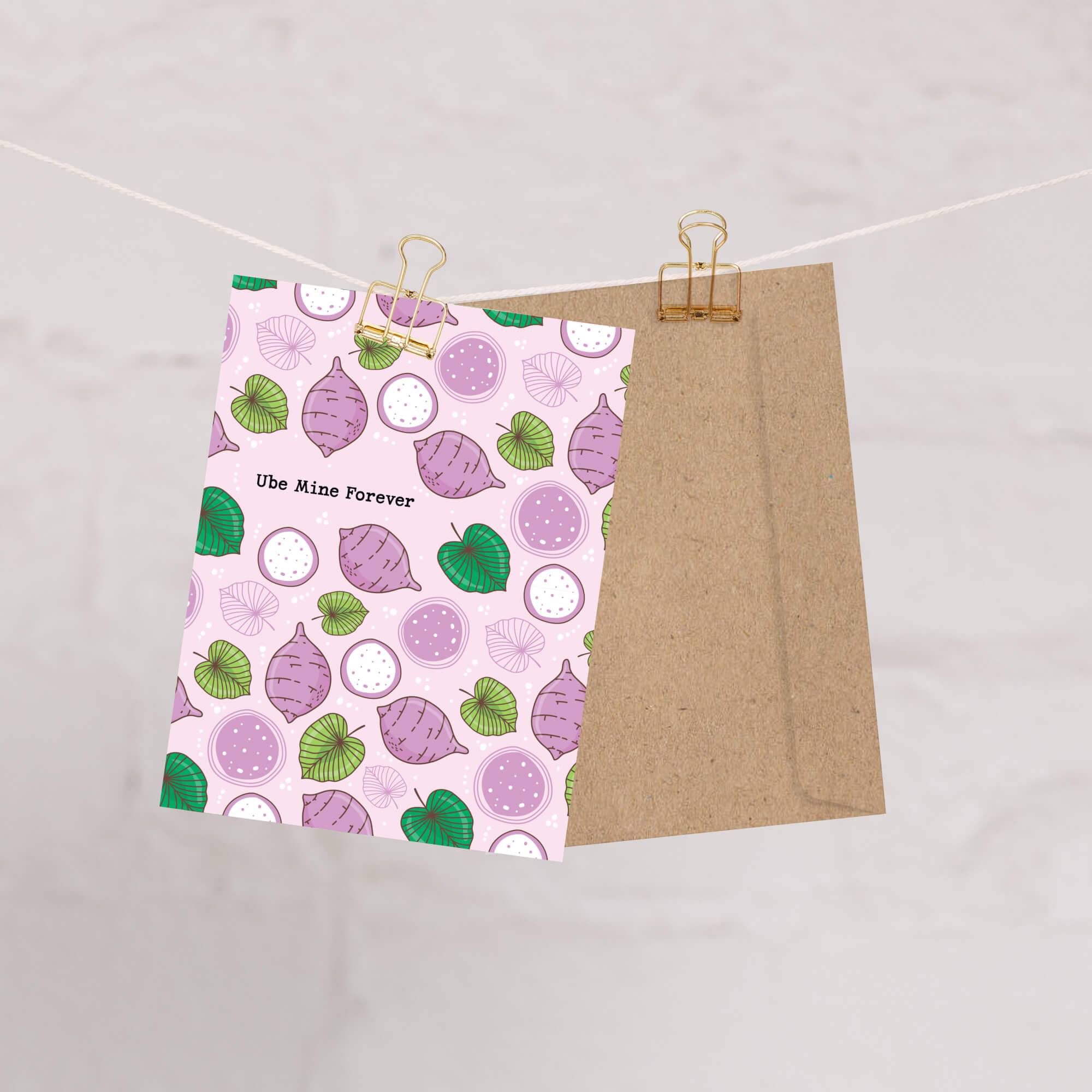 greeting card with a purple and green pattern on a pink background, clipped to a string against a light gray background.