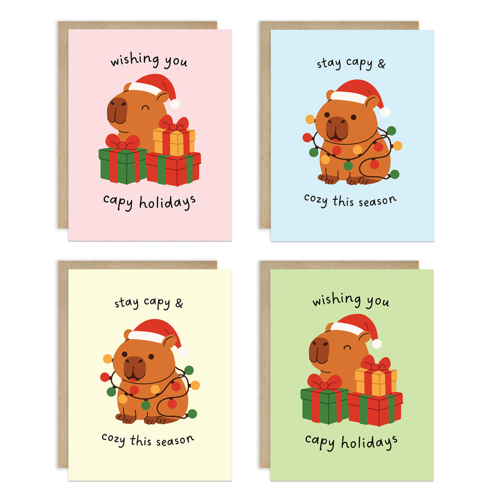 Colorful Capy Holidays card pack showing 4 holiday designs with capybaras in Santa hats, wrapped in string lights or sitting with gift boxes. Each design appears twice for a total of 8 cards with kraft envelopes.