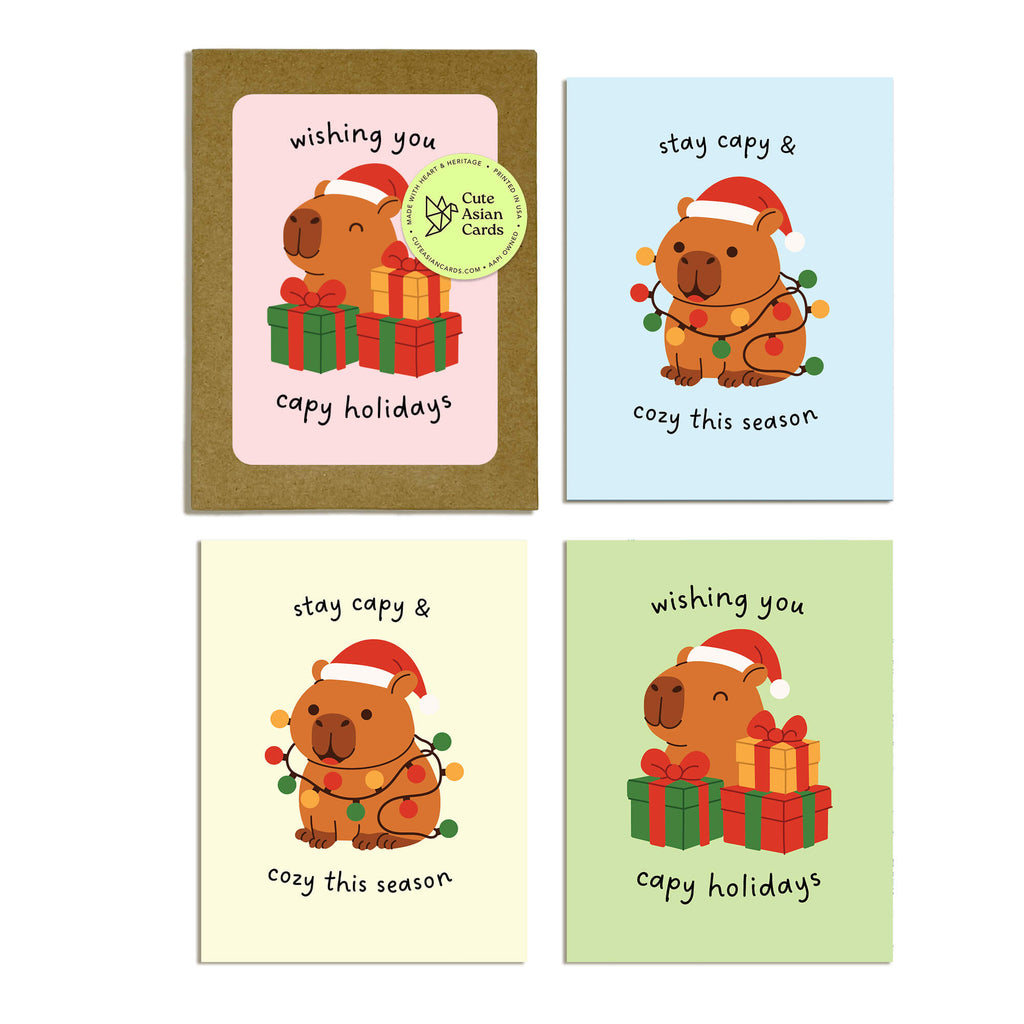 Colorful Capy Holidays card pack showing 4 holiday designs with capybaras in Santa hats, wrapped in string lights or sitting with gift boxes. Each design appears twice for a total of 8 cards with kraft envelopes.