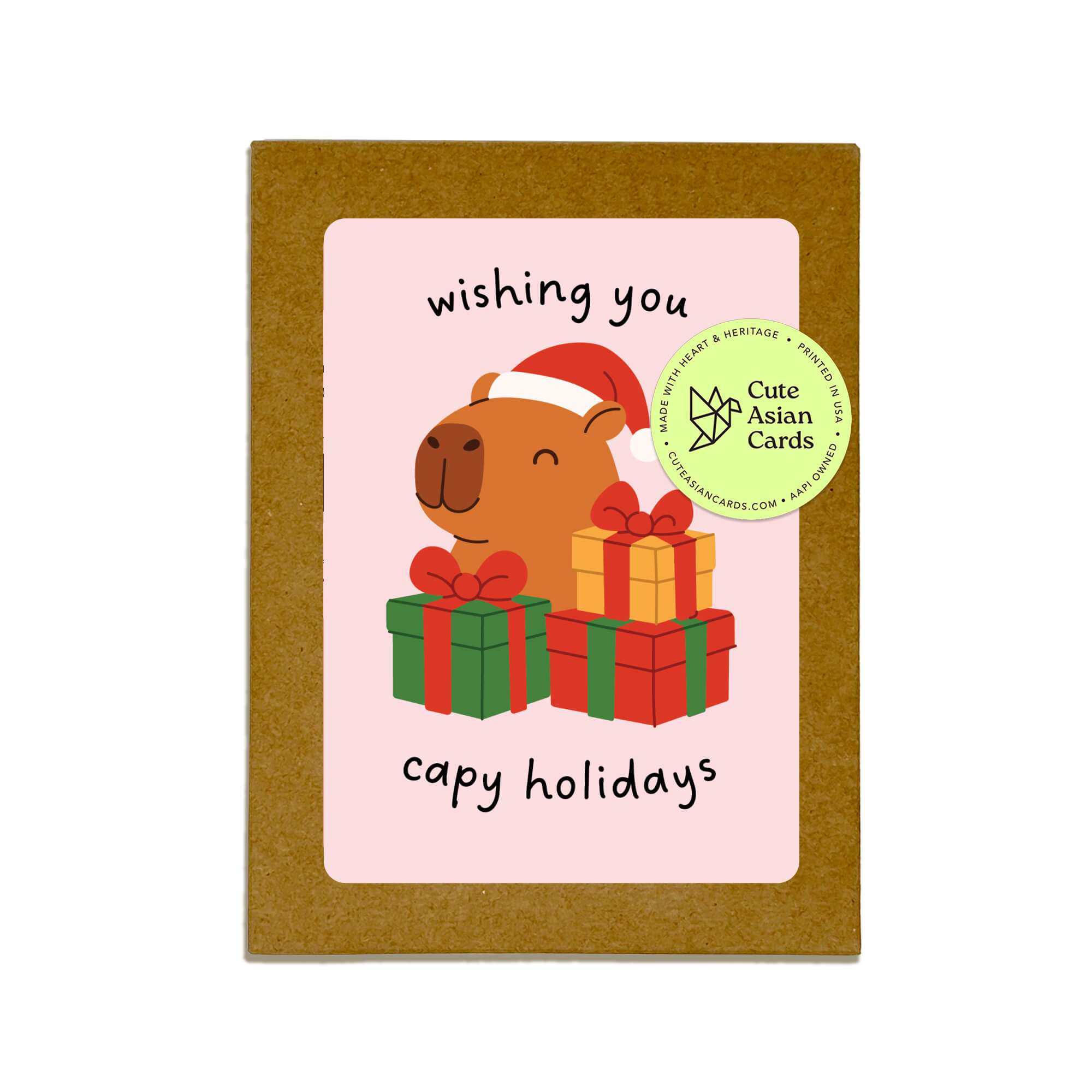 Colorful Capy Holidays card pack showing 4 holiday designs with capybaras in Santa hats, wrapped in string lights or sitting with gift boxes. Each design appears twice for a total of 8 cards with kraft envelopes.