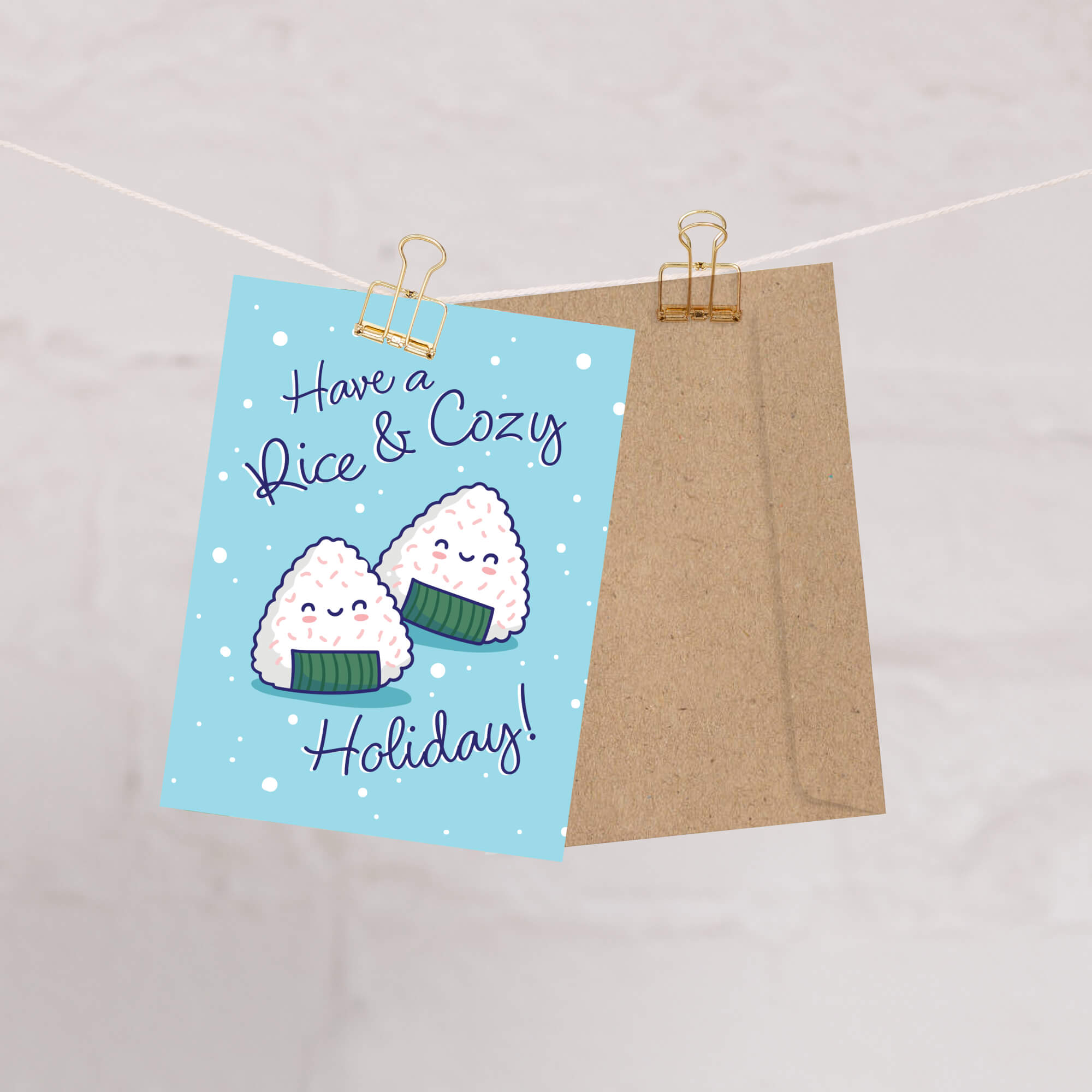 unique christmas card with Two smiling onigiri (japanese rice ball snacks) on snowy blue with text “Have a Rice & Cozy Holiday.”