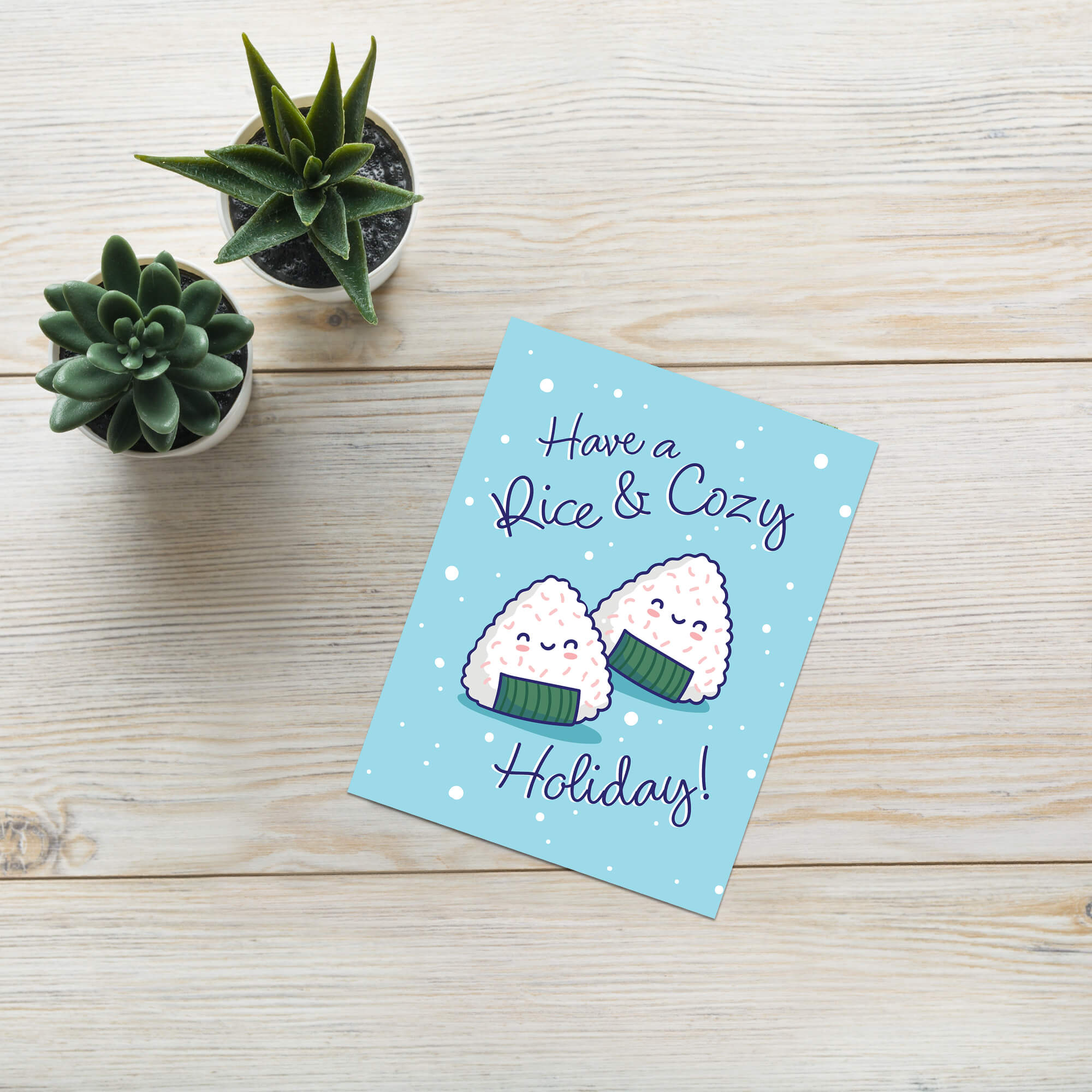 unique christmas card with Two smiling onigiri (japanese rice ball snacks) on snowy blue with text “Have a Rice & Cozy Holiday.”