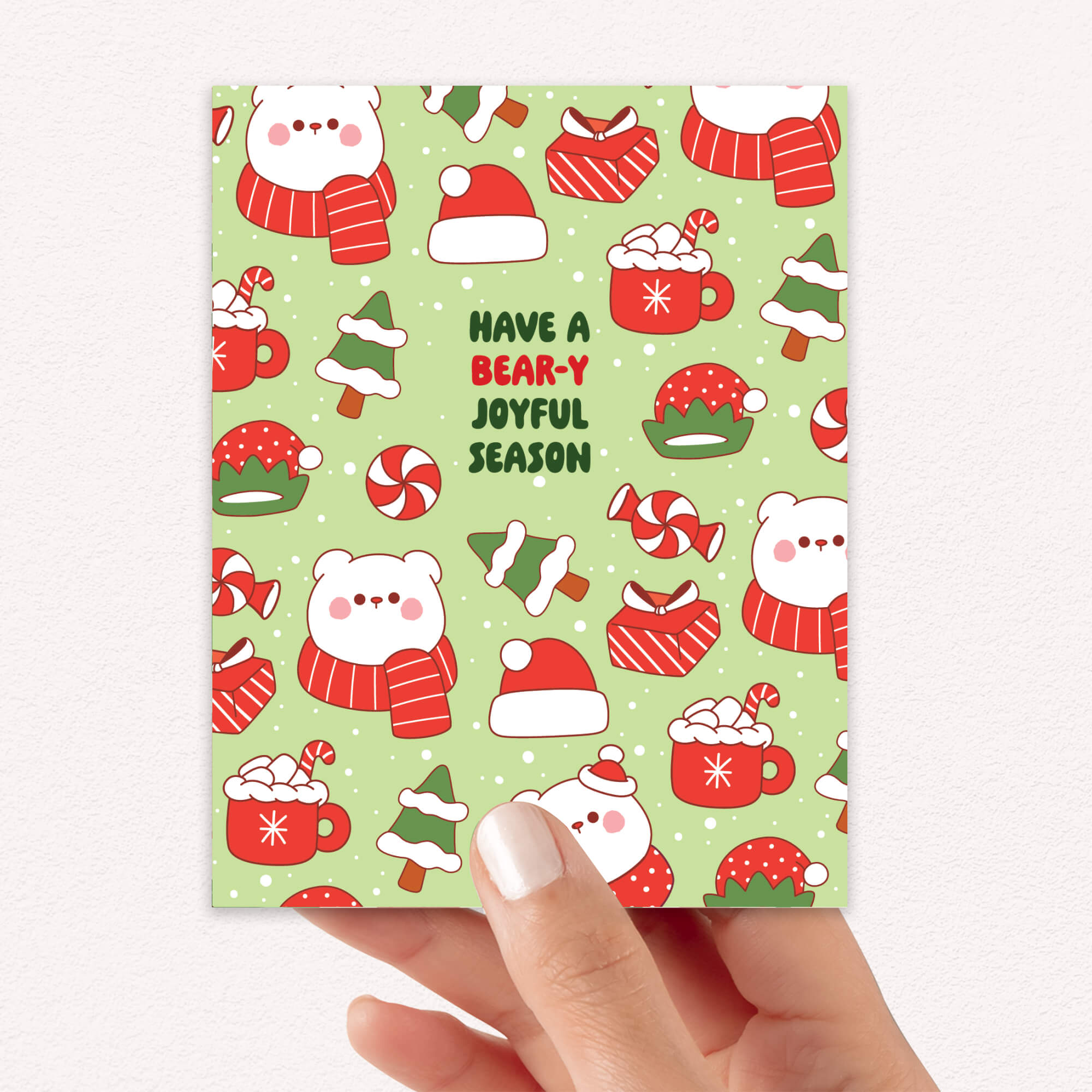 unique Christmas card with white polar bear in red scarf and santa hat and holiday elements on a green background with text "have a bear-y joyful season"