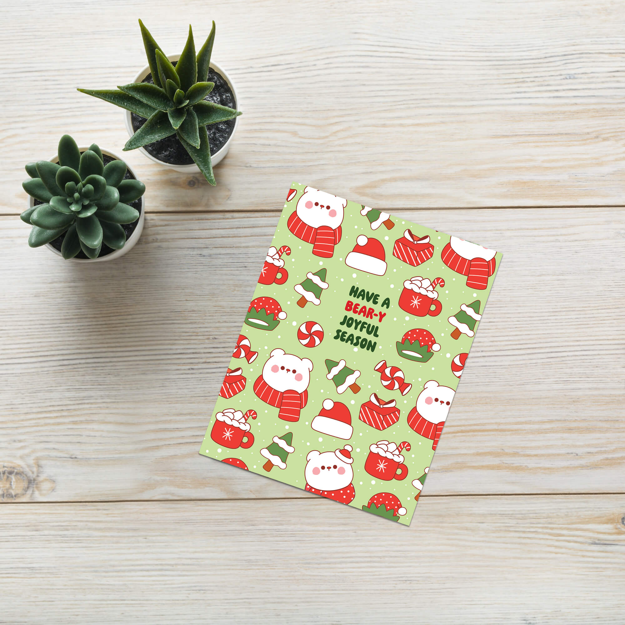 unique Christmas card with white polar bear in red scarf and santa hat and holiday elements on a green background with text "have a bear-y joyful season"