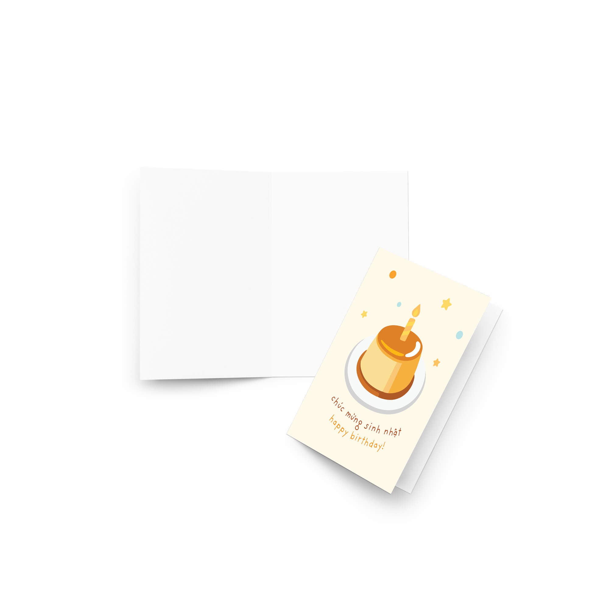A folded Vietnamese birthday card with a cream-colored front featuring a cute illustration of a golden flan or custard dessert on a white plate, with small colorful confetti dots and the French text 'C'est mang aux normes! Happy birthday!' in yellow. The back of the card is plain white and is shown behind the front, all on a clean white background.