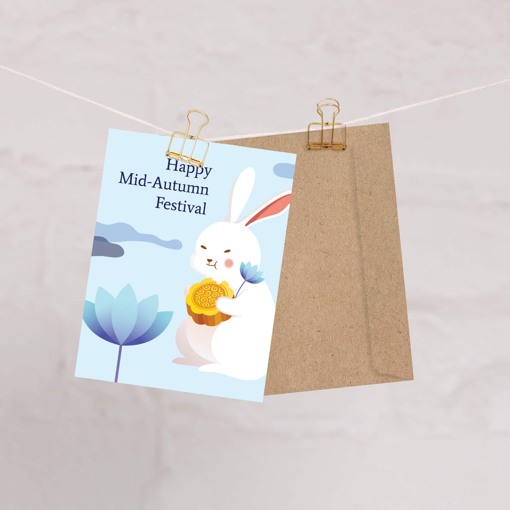 chinese asian Greeting card with a white rabbit holding a mooncake and lotus flower, text 'Happy Mid-Autumn Festival', on a light blue background.