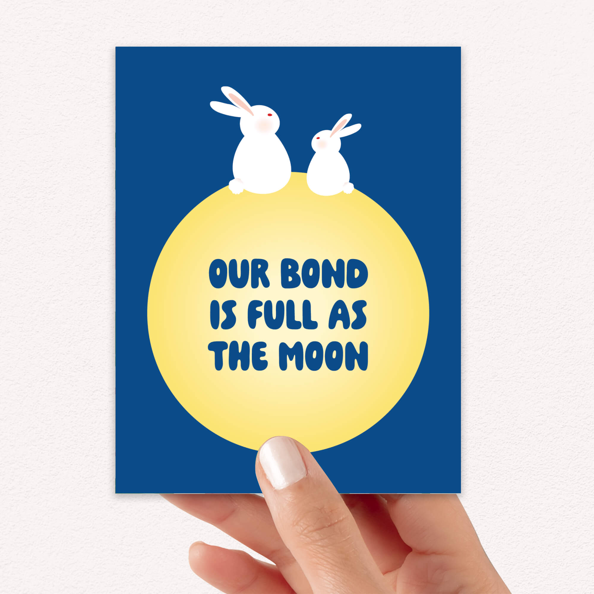 blue asian Greeting card with two rabbits on a yellow moon and 'Our bond is full as the moon' text on a blue background for mid autumn festival tsukimi or chuseok 