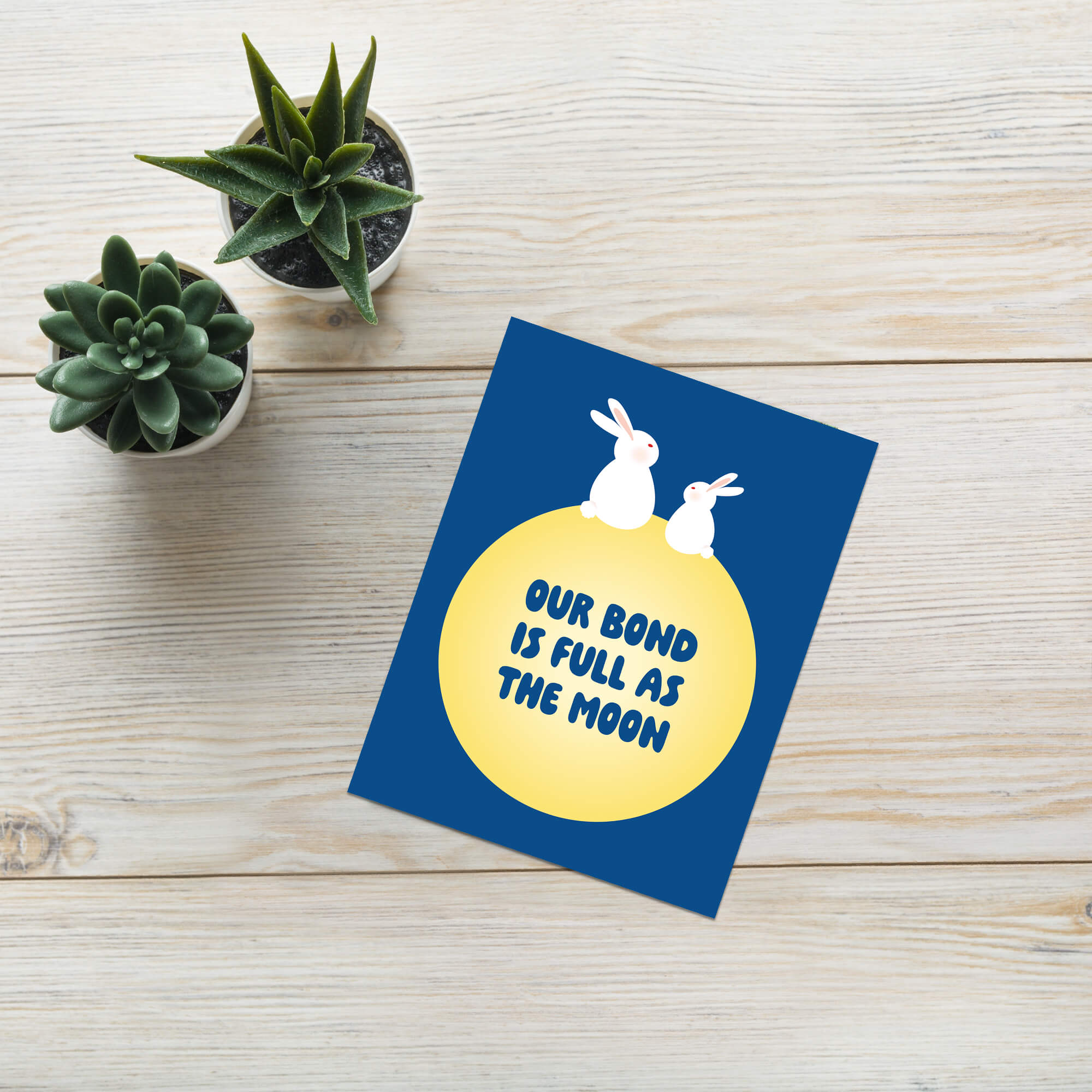 blue asian Greeting card with two rabbits on a yellow moon and 'Our bond is full as the moon' text on a blue background for mid autumn festival tsukimi or chuseok 